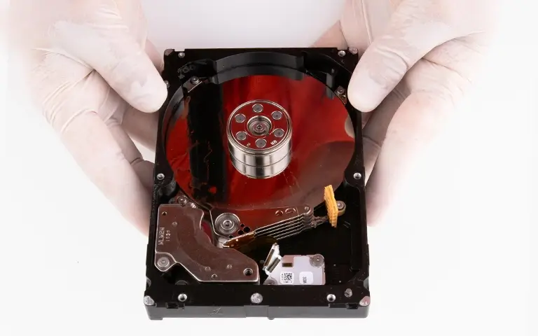 Gloved hands holding an opened hard disk drive exposing the platters and read/write head assembly.